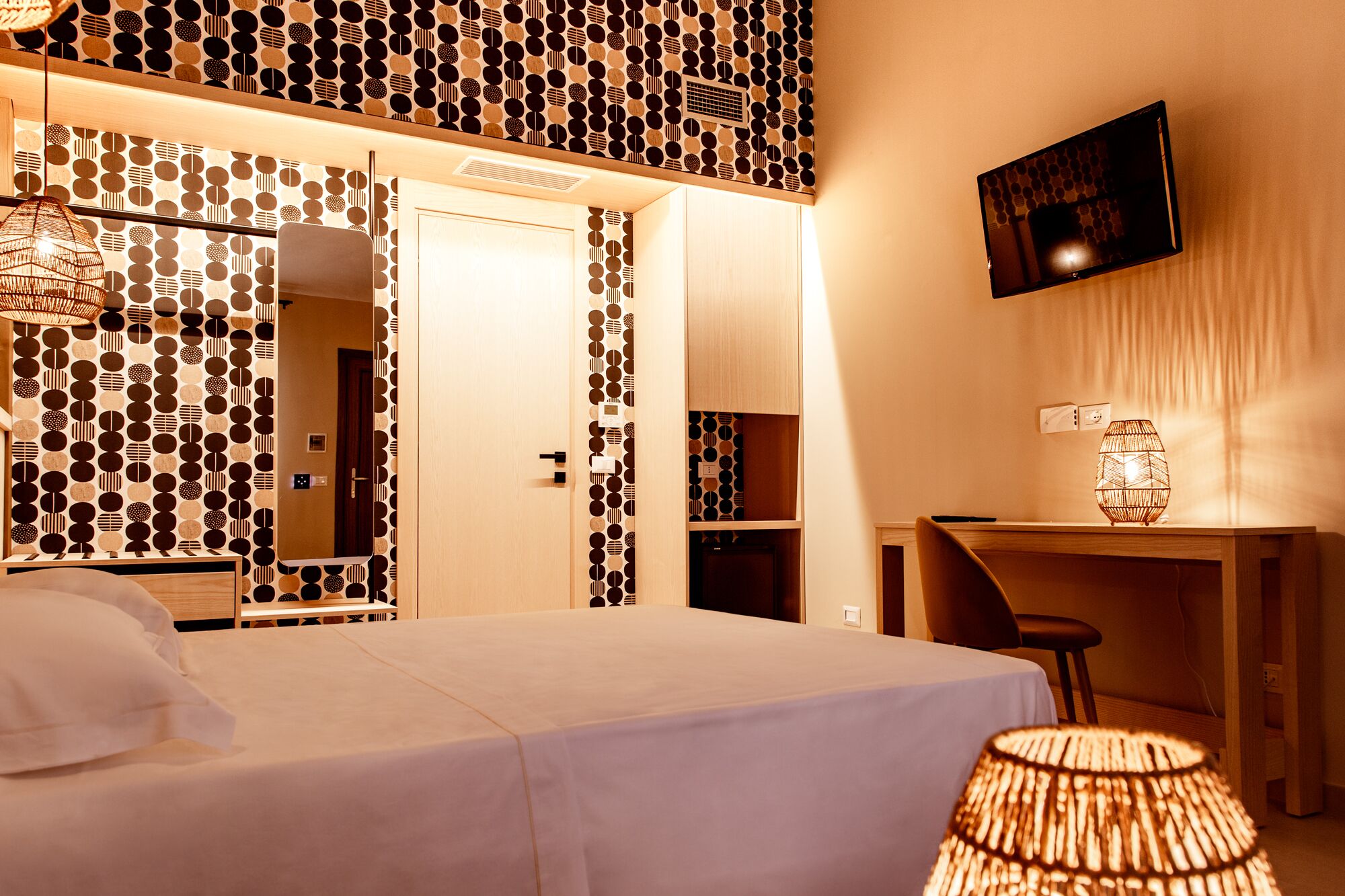 Una habitación de hotel con cama, escritorio, silla, televisor y lámpara.