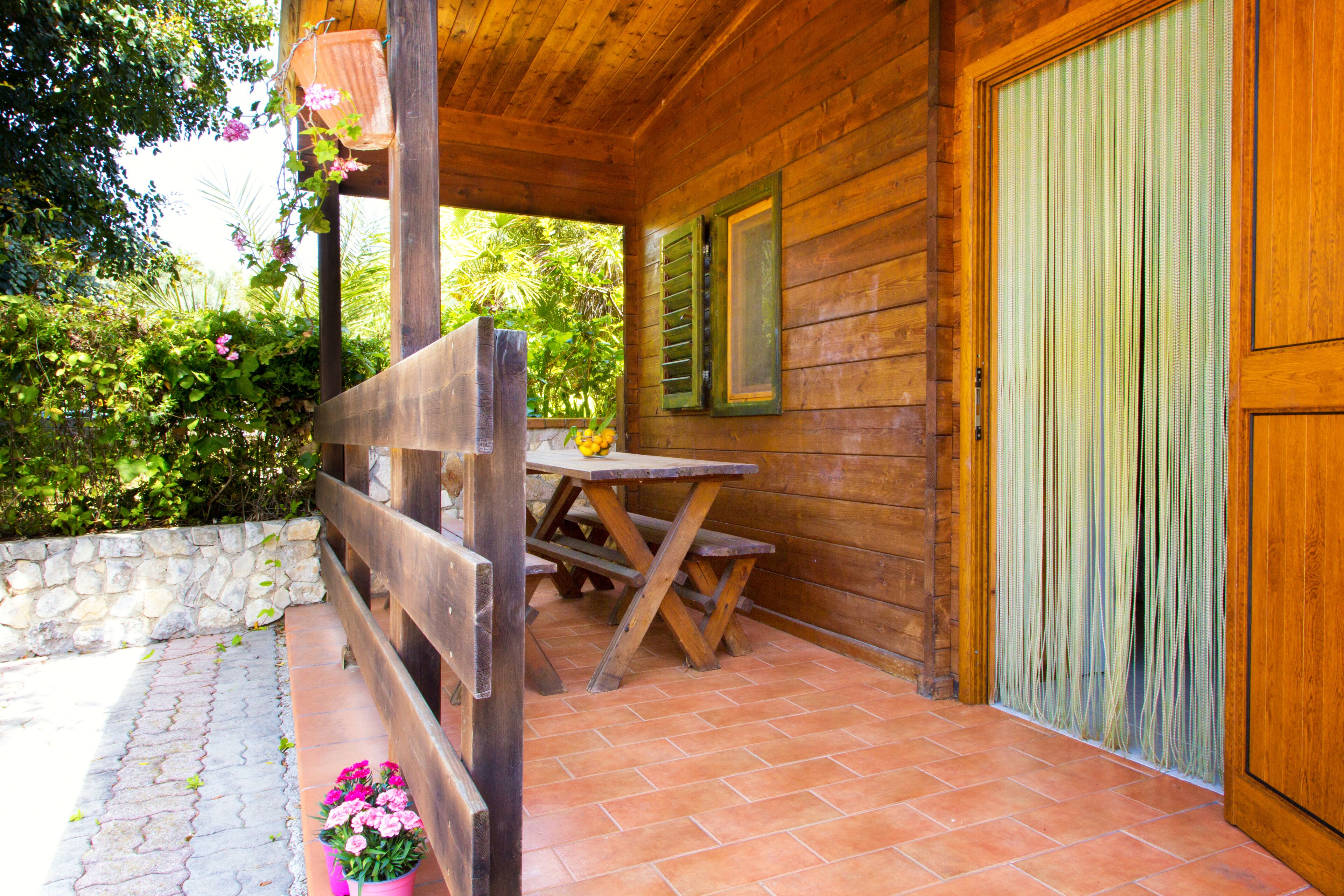 A wooden cabin with a patio area, a stone wall, and a wooden bench.