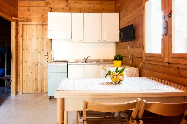 A wooden cabin with a kitchen area, a dining table with chairs, and a small refrigerator. - Albergo Il Giardino (Ischitella)