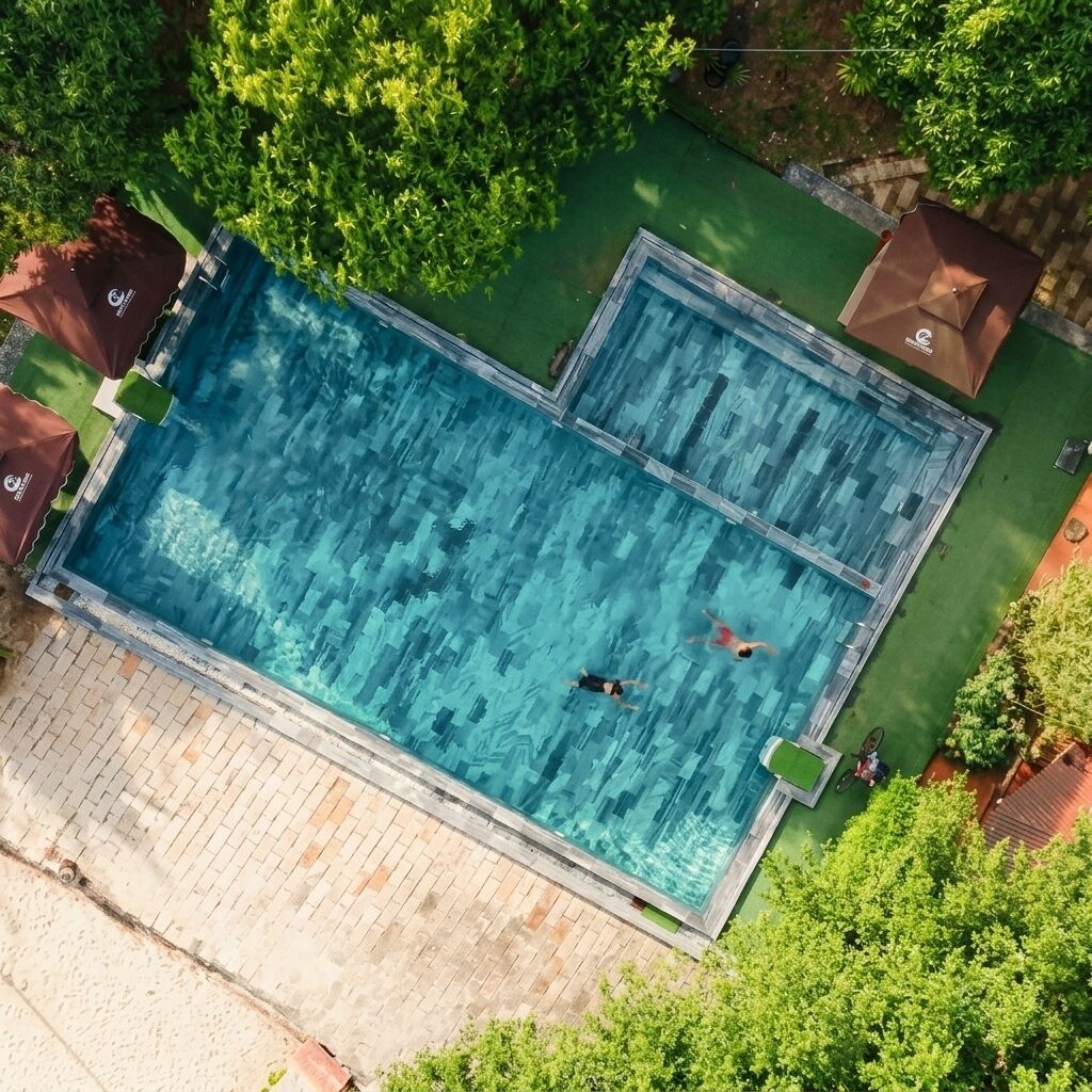Vista aérea de uma piscina retangular com duas pessoas nadando, rodeada por vegetação e um deck pavimentado.