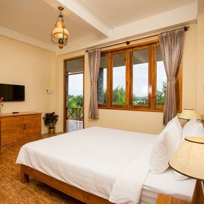 A bedroom with a bed, a television, a wooden dresser, and a window with curtains. - Milana Beach Resort & Spa Phu Quoc (Phu Quoc)
