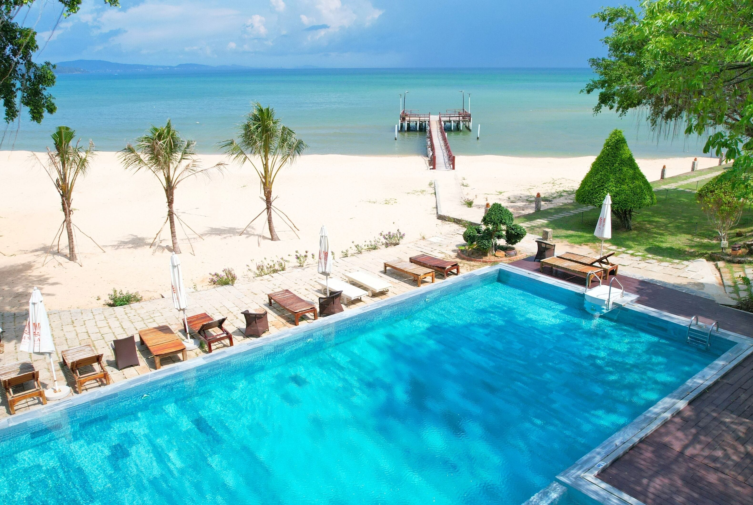 A swimming pool with lounge chairs and a view of the beach and ocean.