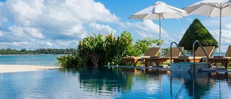 A clear blue pool with lounge chairs and umbrellas, surrounded by tropical plants and a view of the beach.