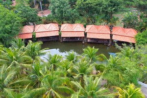 A row of bungalow-style accommodations with thatched roofs, situated adjacent to a body of water, surrounded by lush greenery.