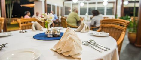 A dining area with tables set for two, featuring white tablecloths, silverware, and a blue placemat.