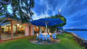 An outdoor dining area with tables and chairs, a blue umbrella, and a view of the water. - Madang Resort (Madang)
