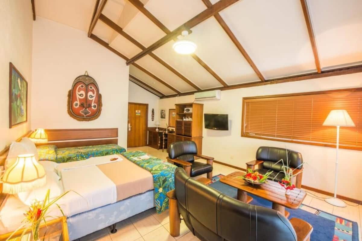 Ein Zimmer mit einem Bett, zwei Sesseln, einem Schreibtisch, einer Lampe und einem Fernseher.