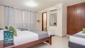 A hotel room with two beds, a wooden wardrobe, a mirror, and an air conditioning unit.