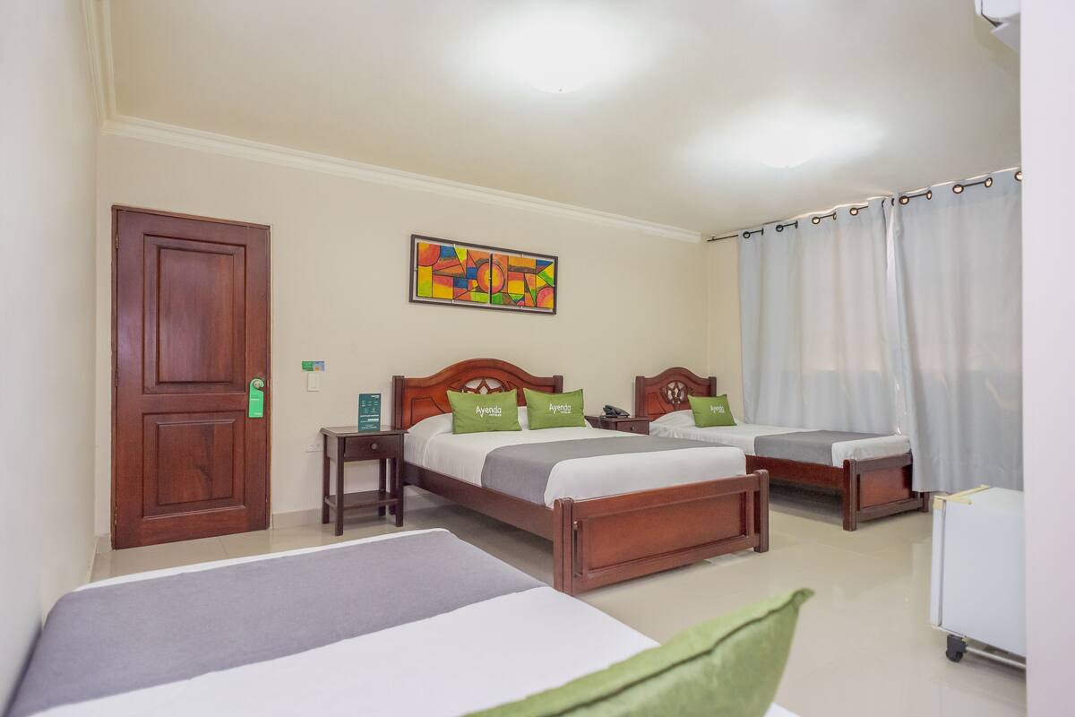 Habitación de hotel con dos camas, cabecera de madera, mesita de noche y un cuadro abstracto colorido en la pared.