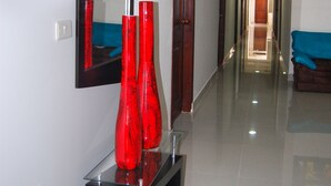 A hallway with a mirror, a black console table with red vases, and a blue sofa.