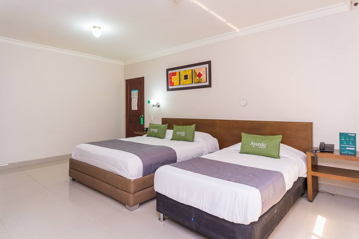 Habitación de hotel con dos camas, cabecero de madera, mesita de noche con teléfono y un cuadro en la pared.