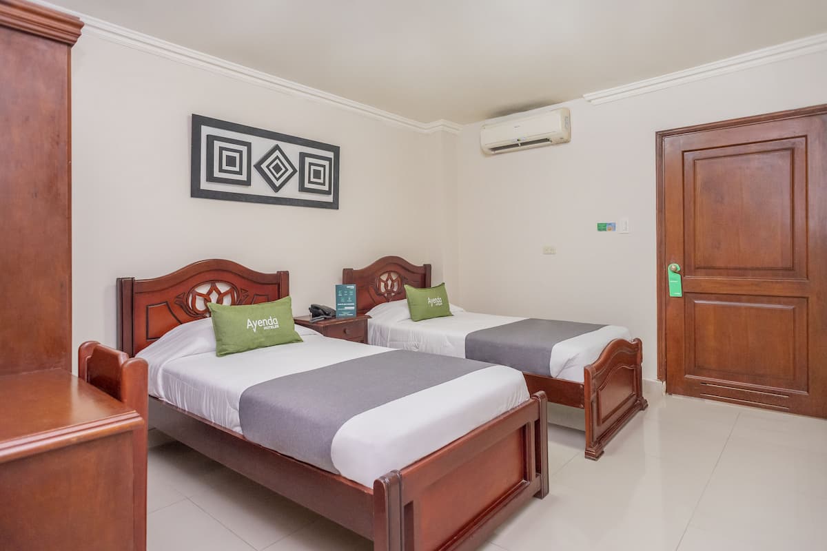 Una habitación de hotel con dos camas de madera, una mesita de noche, aire acondicionado montado en la pared y una puerta de madera.