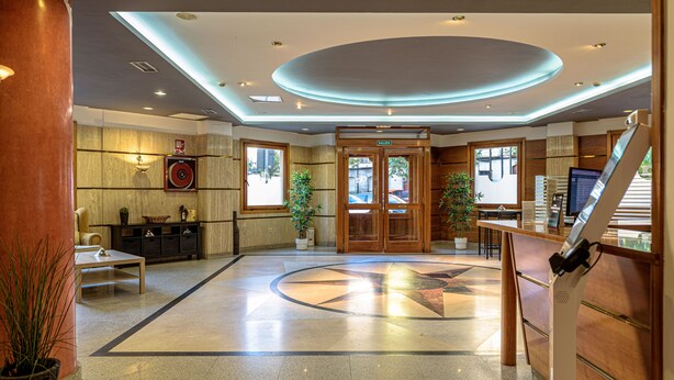A hotel lobby with a reception desk, a large circular floor design, and a wooden door leading to the exit. - Alda Ciudad de Toro (Toro)