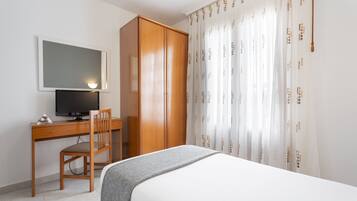 Un dormitorio con cama, escritorio con silla, televisor y armario.