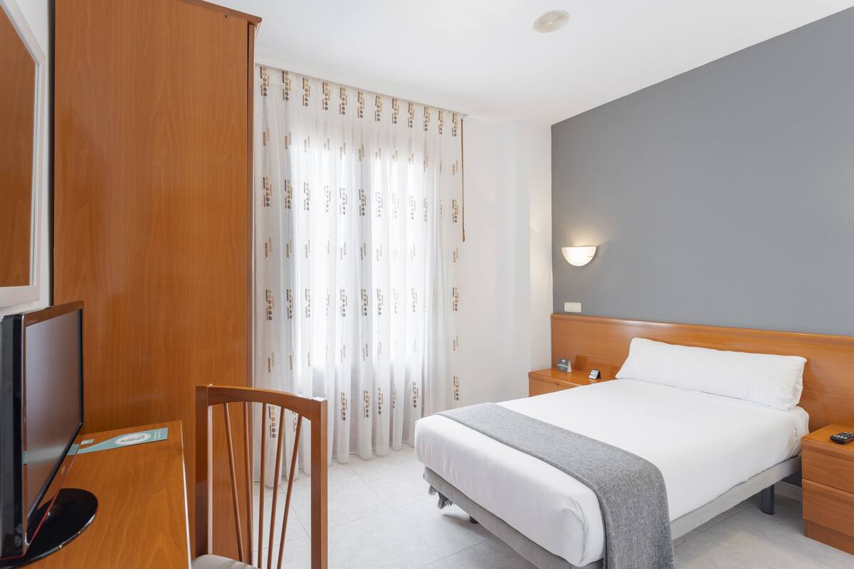 A hotel room with a bed, bedside tables, a TV, and a chair.