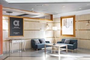 A modern hotel lobby with a reception desk, two sofas, a coffee table, and a large framed logo on the wall. - Alda Ciudad de Toro (Toro)