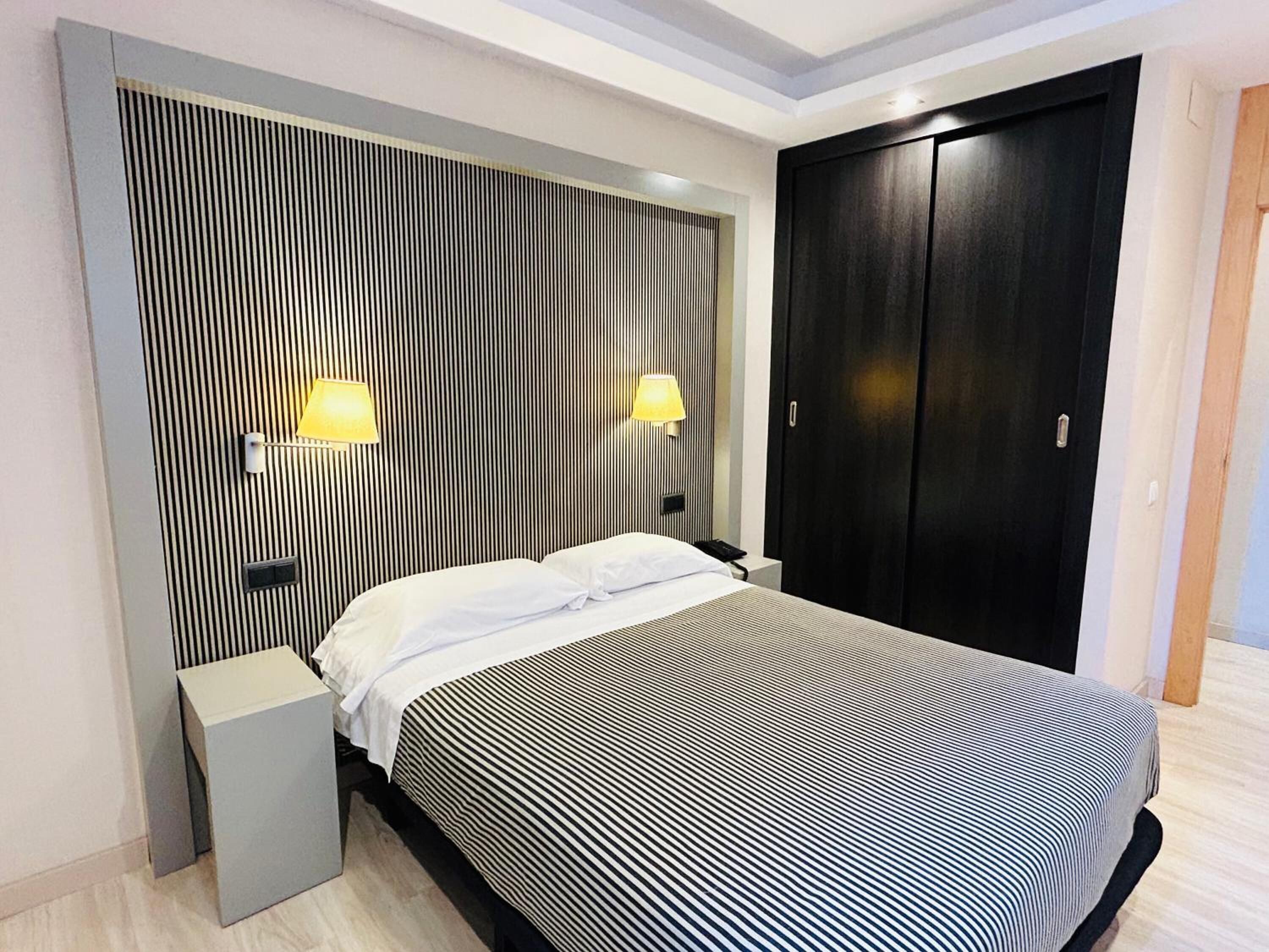 A modern bedroom with a bed, bedside tables, a wardrobe, and wall-mounted lamps.