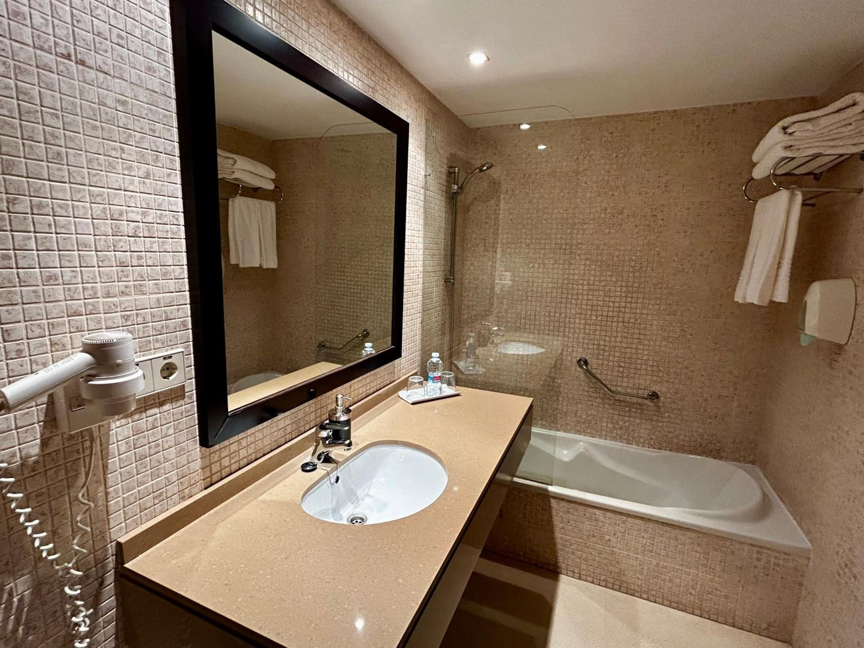 A bathroom with a large mirror, a sink, a bathtub, and a shower.