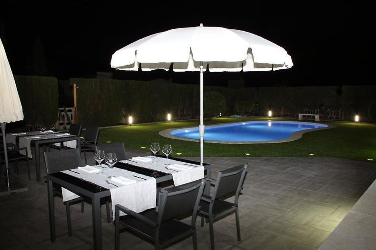 An outdoor dining area with tables and chairs, a pool, and an umbrella.