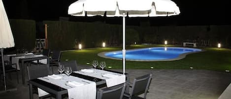 An outdoor dining area with tables and chairs, a pool, and an umbrella.