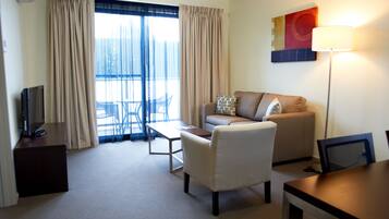 A hotel room with a sofa, armchair, TV, and a dining table.