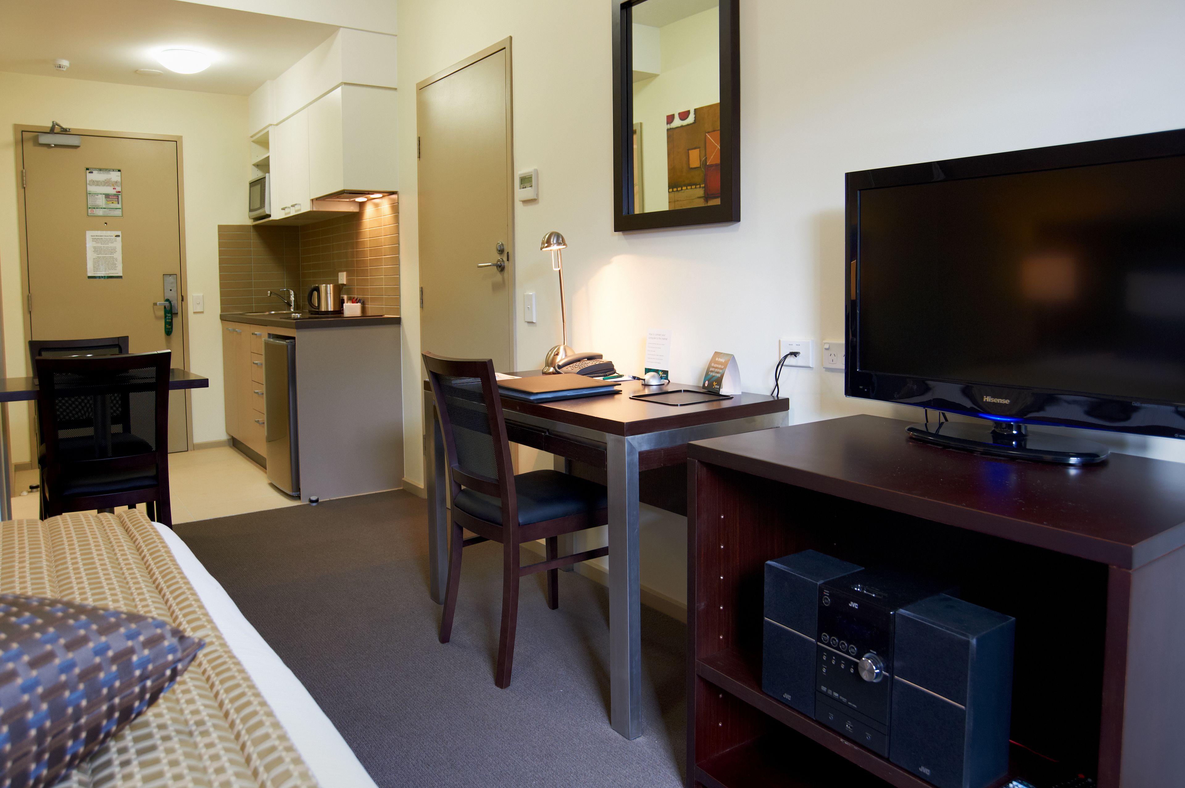 Habitación de hotel con cama, escritorio con silla, televisión, microondas y una pequeña kitchenette.