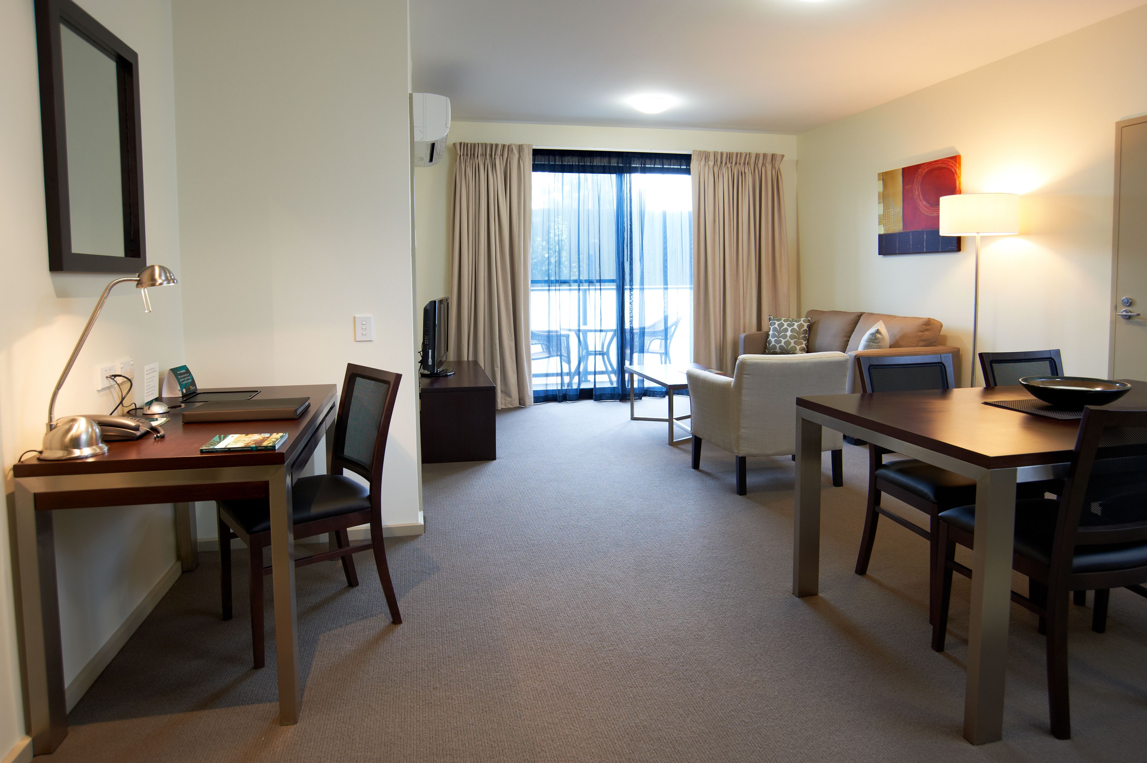 A hotel room with a desk, chairs, a sofa, a dining table, and a balcony with a view.