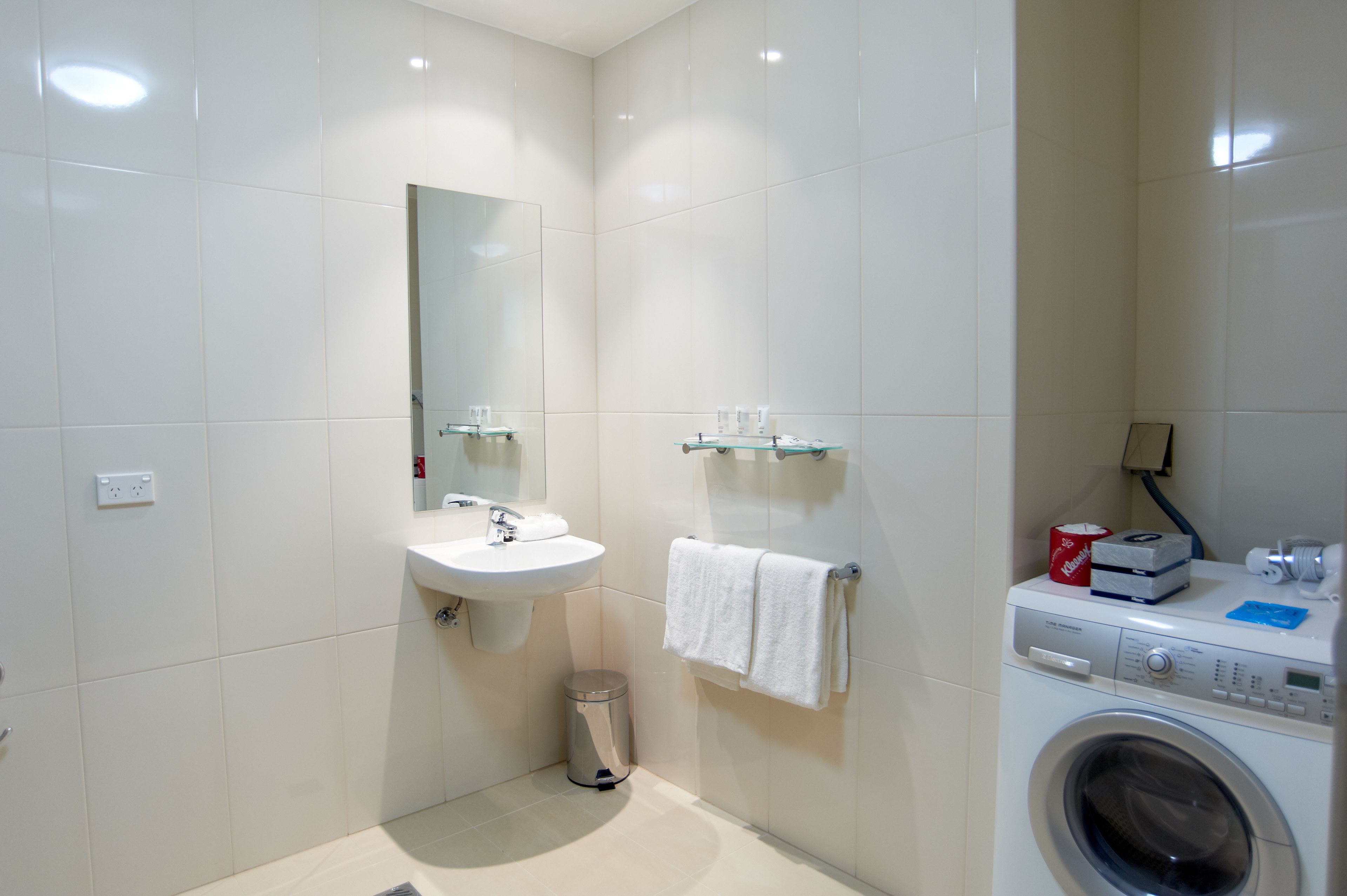 Ein modernes Badezimmer mit Waschbecken, Spiegel, Handtuchhalter und einer Waschmaschine.
