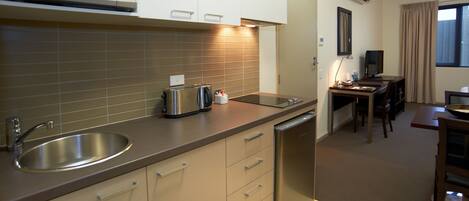 Cocina compacta con microondas, fregadero y lavavajillas. Cuenta con una zona de comedor con mesa y sillas.