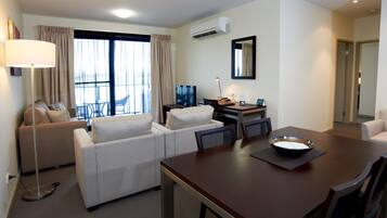 A hotel room with a dining area, a sofa set, a desk with a computer, and a large window with curtains.