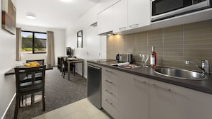Una cocina moderna con armarios blancos, un lavamanos de acero inoxidable y un microondas. Hay un comedor con una mesa y sillas, y una ventana con cortinas.