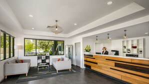 Una moderna zona de recepción con un mostrador de madera, un espacio de estar con sofás y ventanas grandes que ofrecen vistas al exterior.