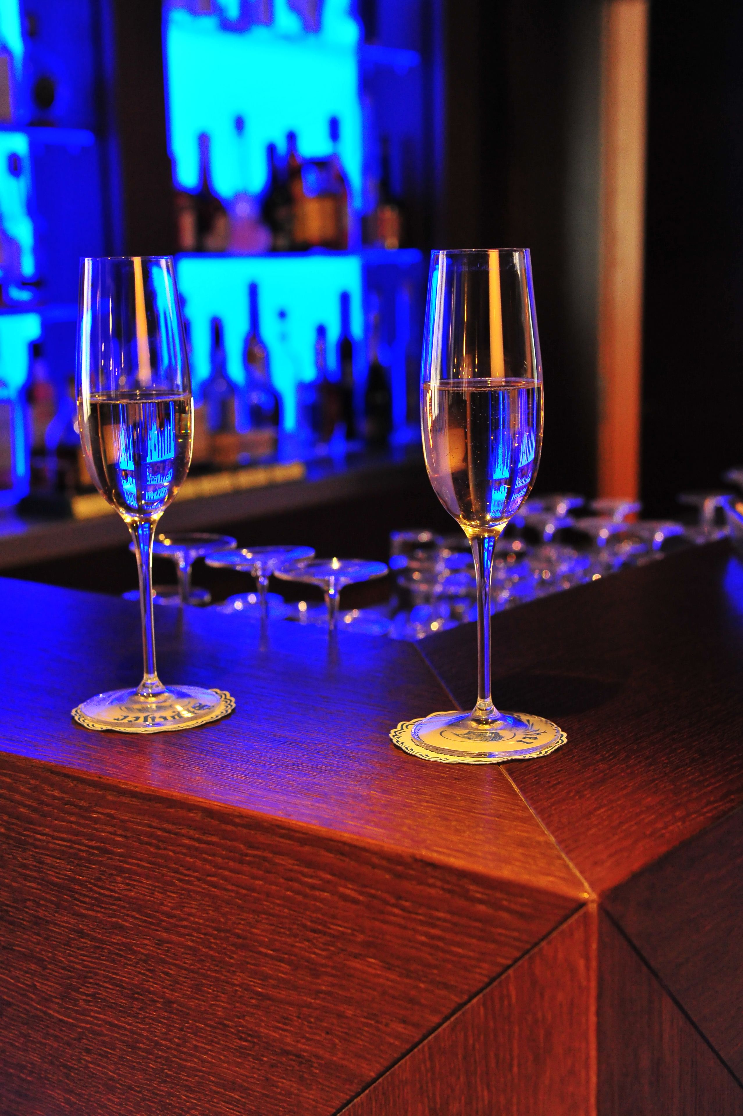 Two empty wine glasses on a bar counter with a blue-lit background.