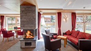 A modern living room with a fireplace, red furniture, and large windows offering a view of the outdoors. - Aristella Swissflair Hotel & Apartements (Zermatt)