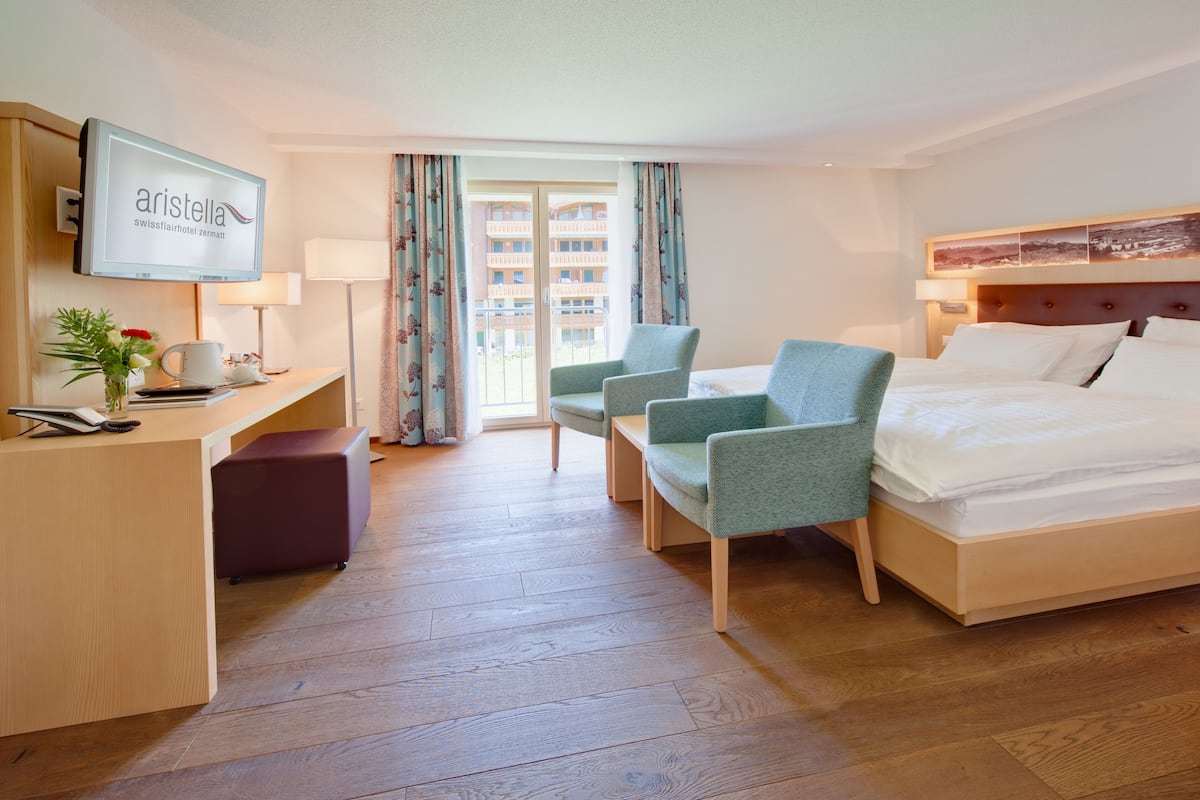 Habitación de hotel con cama, escritorio con computadora, una silla y televisor mostrando el nombre del hotel.