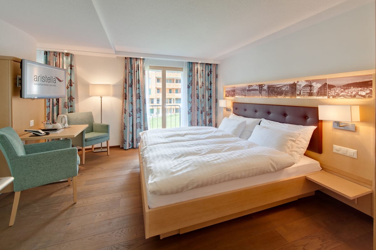 Una habitación de hotel con cama, escritorio con silla, televisor y ventana con cortinas.