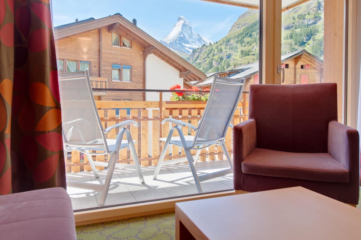 Un balcón con dos sillas, una mesa y vistas a una montaña y edificios de madera.