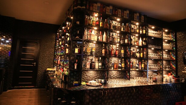 Una zona de bar con estantes llenos de botellas y vasos, una barra de madera y una puerta.