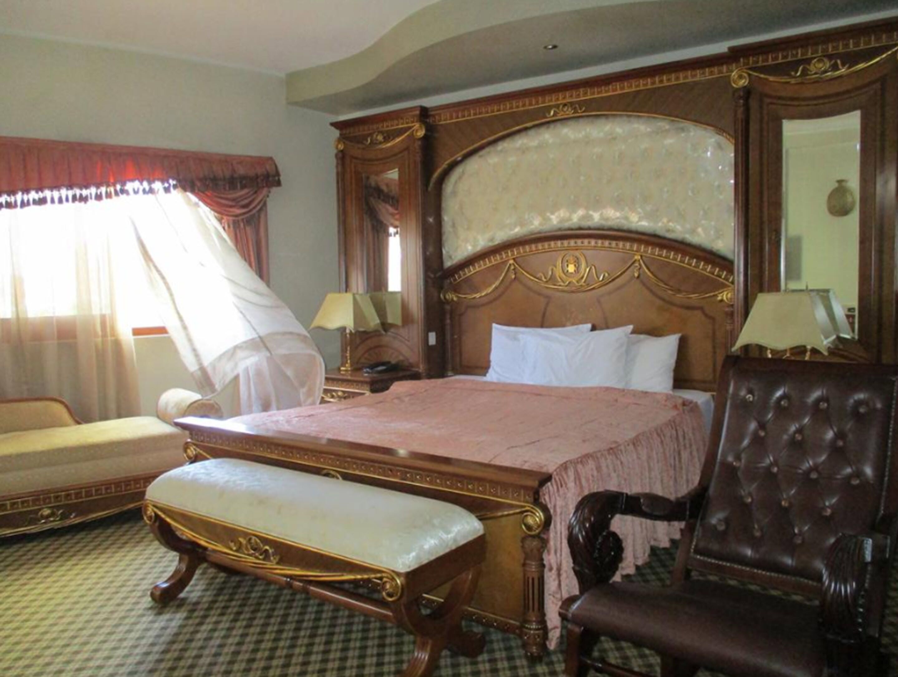 A hotel room with a large bed, a sitting area with a bench, a chair, and a large mirror.