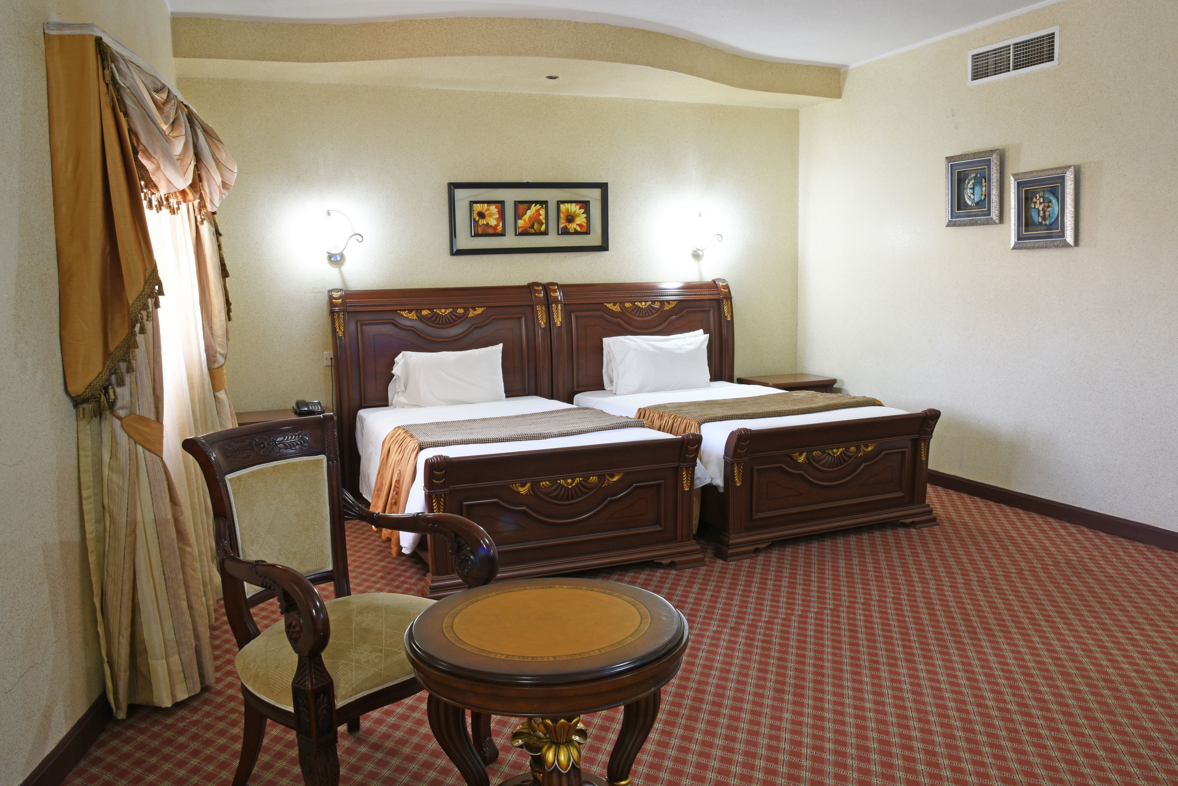 Una habitación de hotel con una cama doble, una silla de madera, una mesita redonda y una alfombra a cuadros.