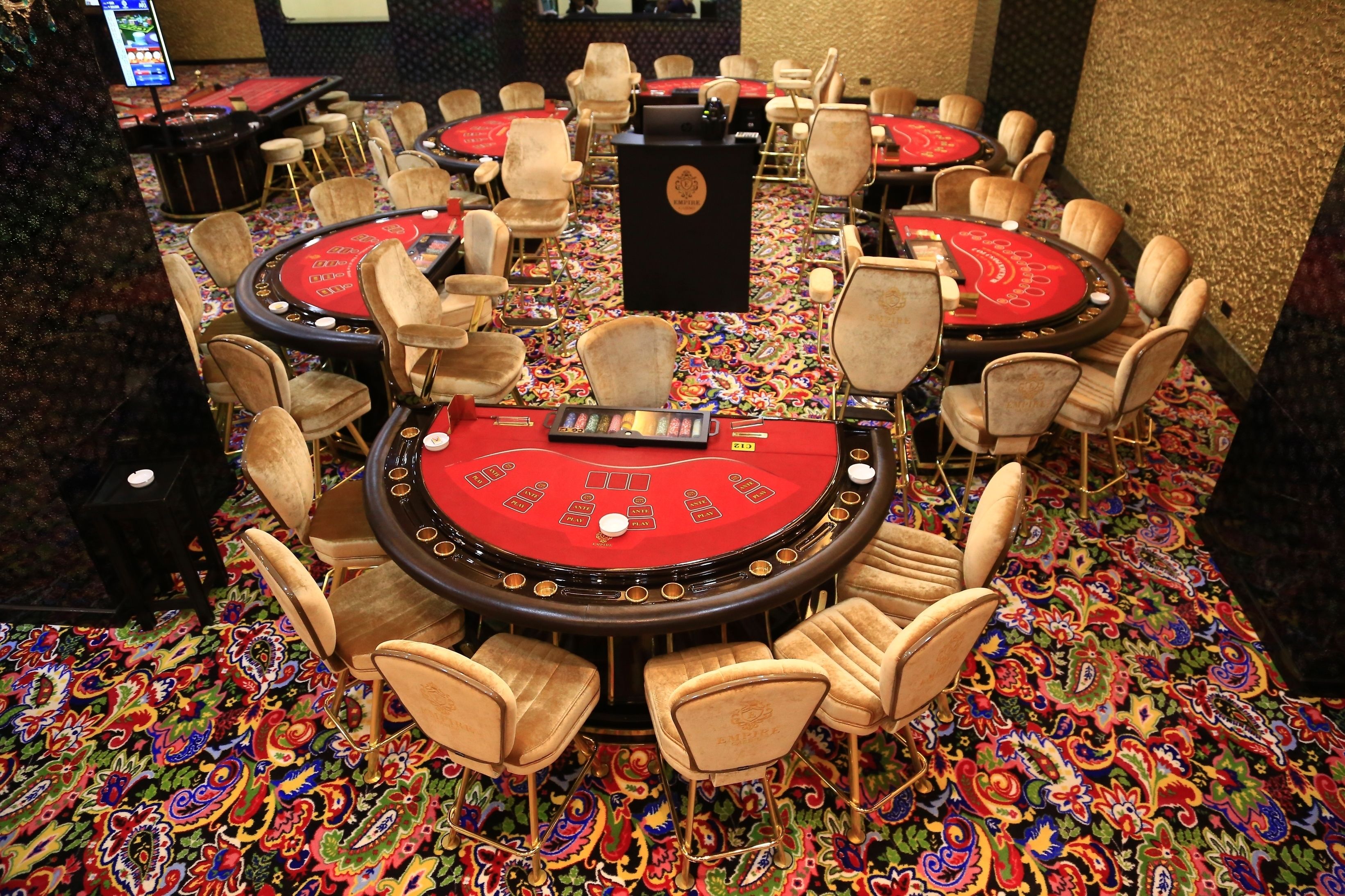 A casino floor with multiple blackjack tables, each surrounded by chairs, and a carpeted floor with a colorful pattern.