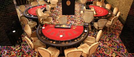 A casino floor with multiple blackjack tables, each surrounded by chairs, and a carpeted floor with a colorful pattern.