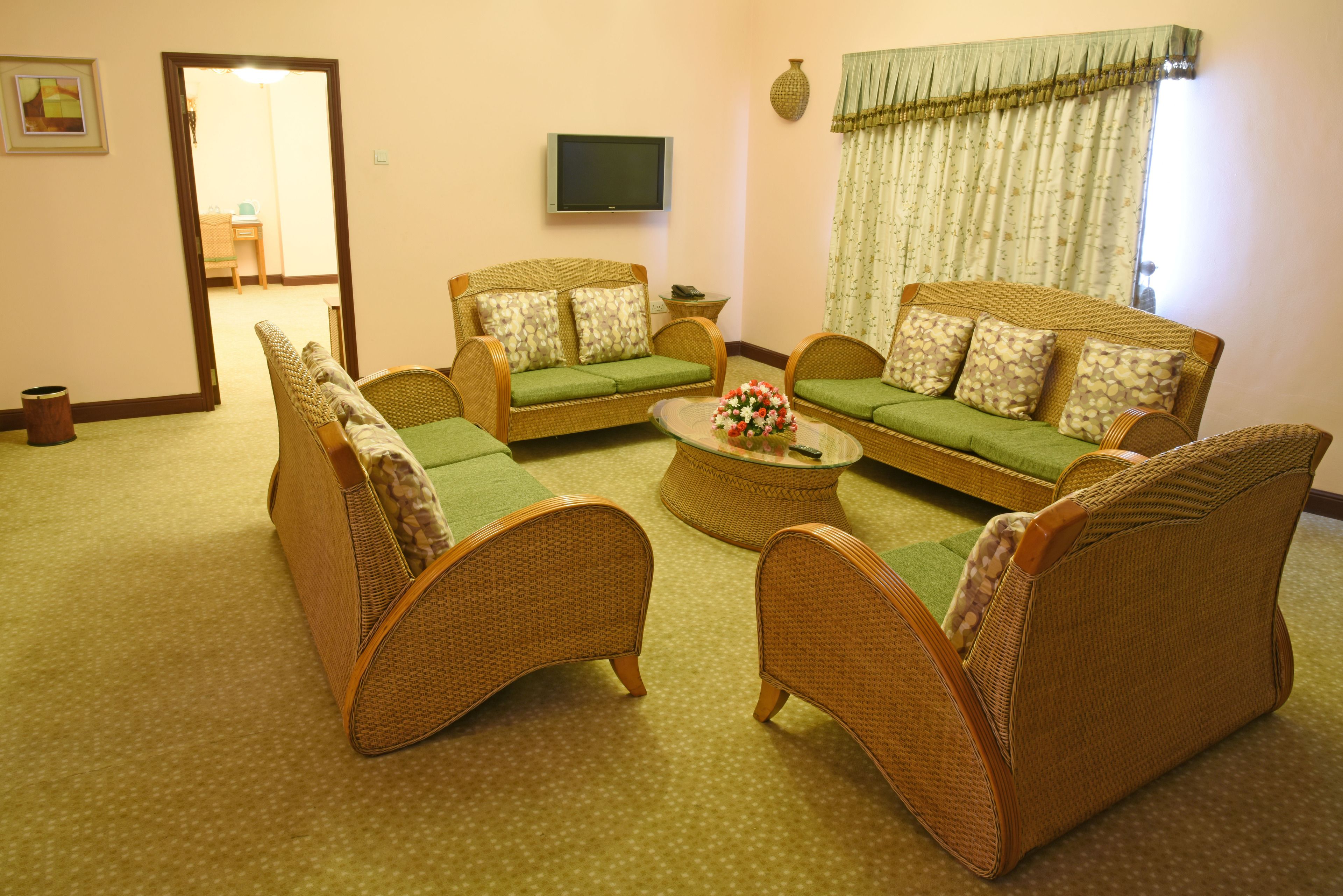 A living room with wicker furniture, a flat-screen TV, and a window with curtains.
