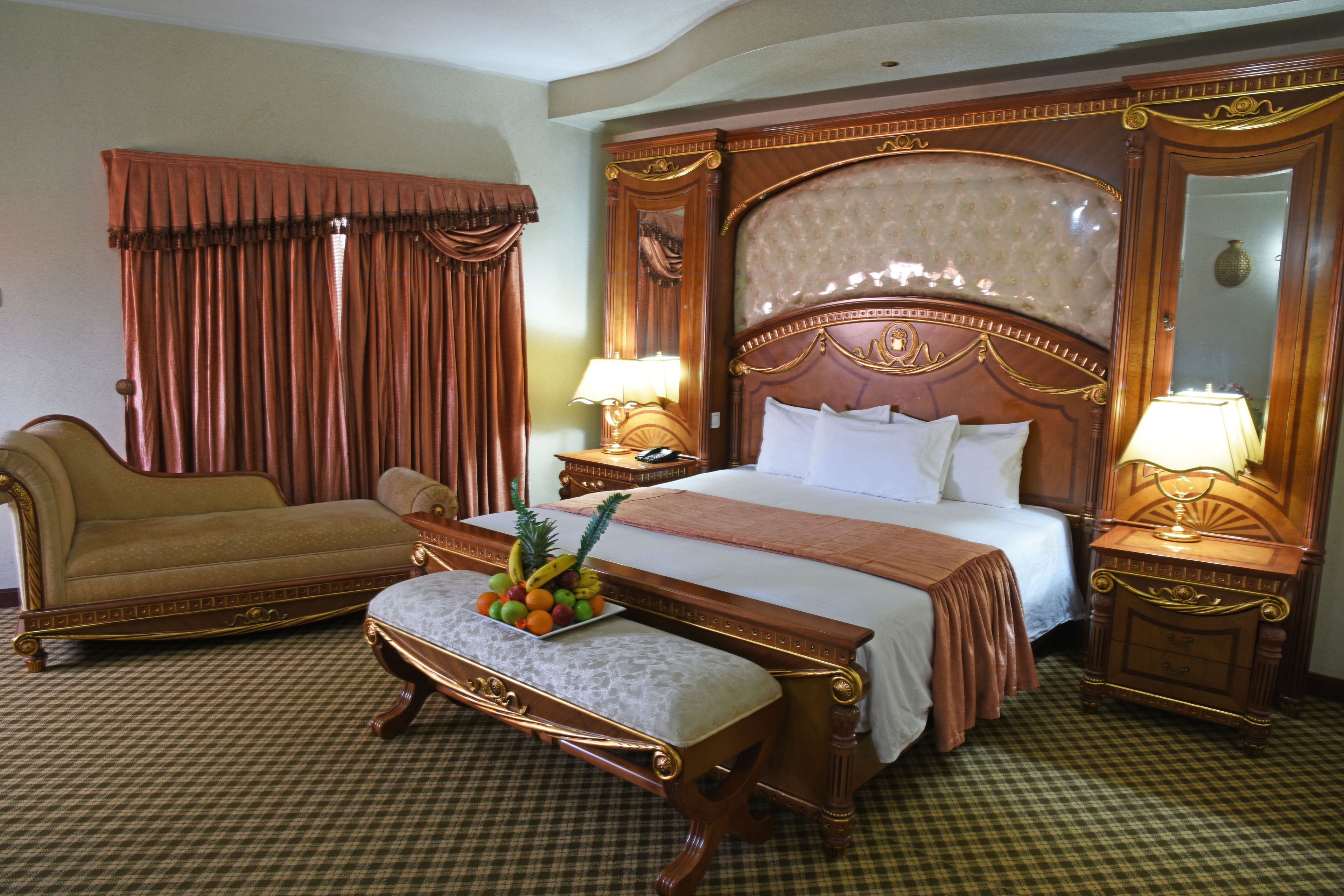 A hotel room with a large bed, a sofa, a bedside table with a lamp, and a mirror.