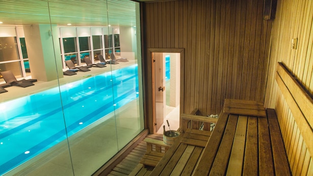 A wooden sauna room with a glass wall overlooking a pool area. - The Landmark Hotel (Baku)