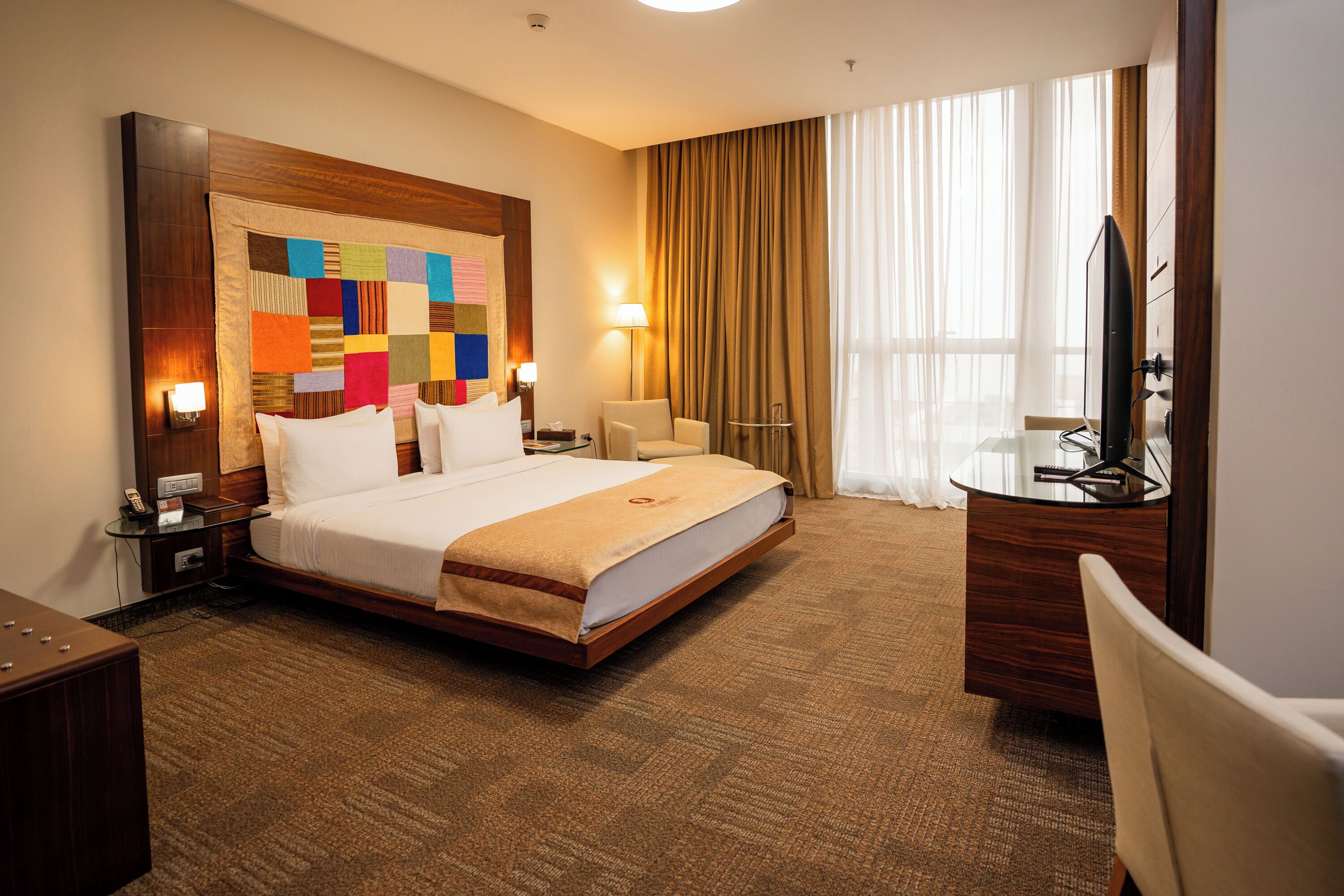 Een hotelkamer met een groot bed, een bureau met computer, een stoel, een televisie en een raam met gordijnen.