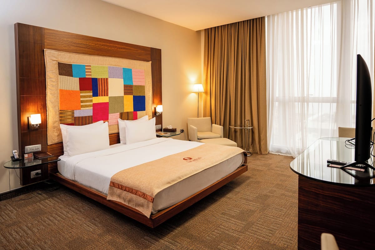 A hotel room with a large bed, a desk with a TV, a chair, and a window with curtains.
