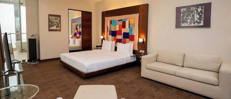 A hotel room with a bed, a sofa, a glass table, and a TV.