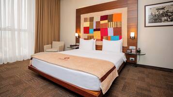 A hotel room with a large bed, a wooden headboard, a colorful quilt, a nightstand, a lamp, and a framed picture on the wall.