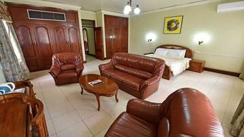 Una sala de estar con sofá, sillón, mesa de centro y una cama con mesita de noche.
